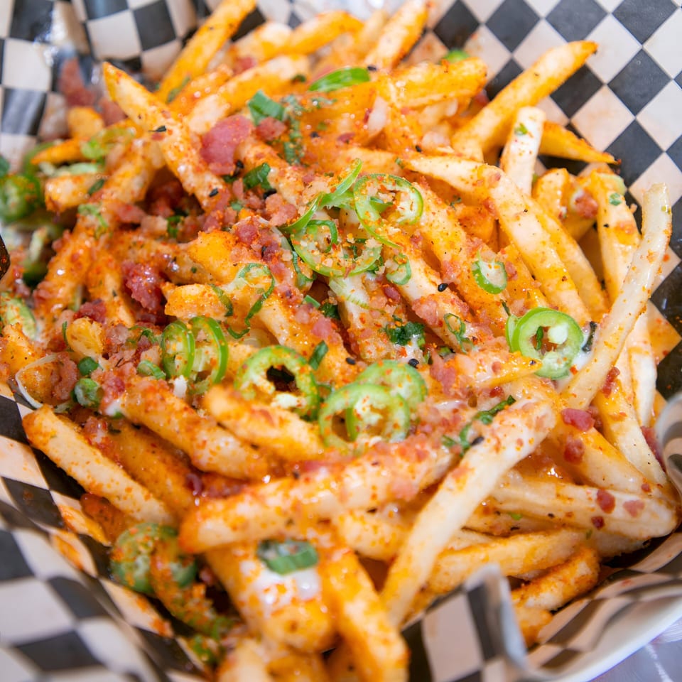 Close-up of Knockout Wings' loaded fries with cheese, bacon bits, and sliced jalapeños in a checkered paper.