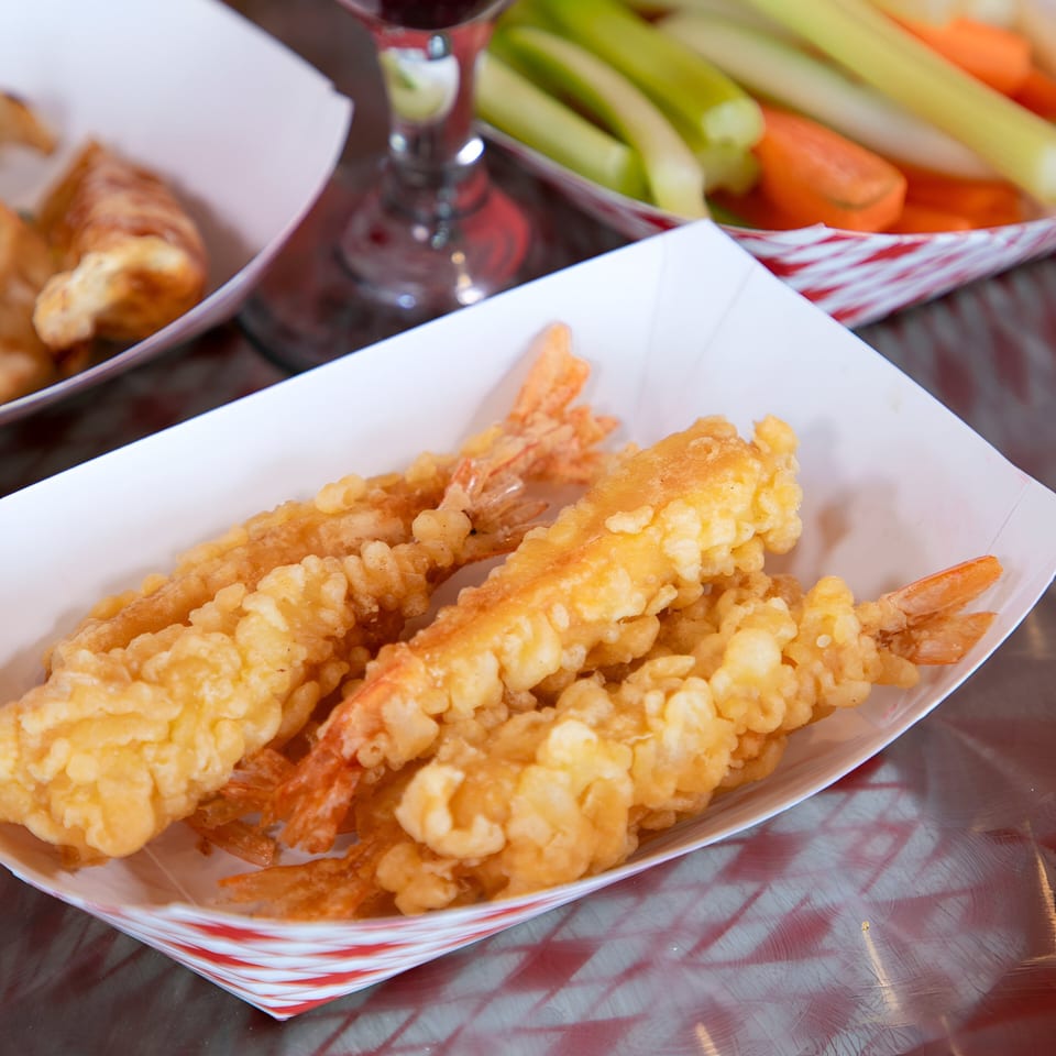 Crispy fried shrimp in a white paper tray with red stripes, alongside celery and carrots.