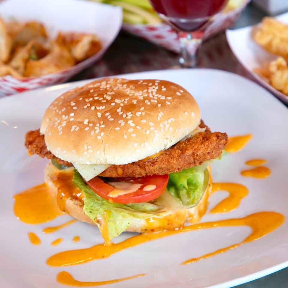 A Knockout Wings fried chicken sandwich with lettuce, tomato, and sauce on a white plate.