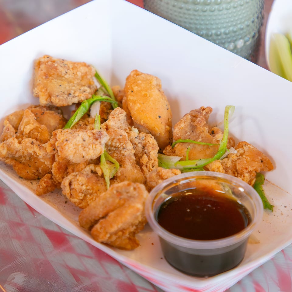 Crispy fried chicken pieces with green onions and a side of dark dipping sauce in a white container.