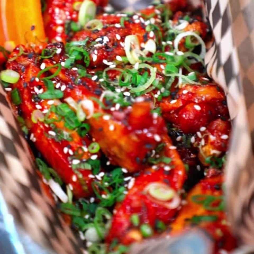Close-up of Knockout Wings' fast-food chicken wings, coated in red sauce, sesame seeds, and green onions.