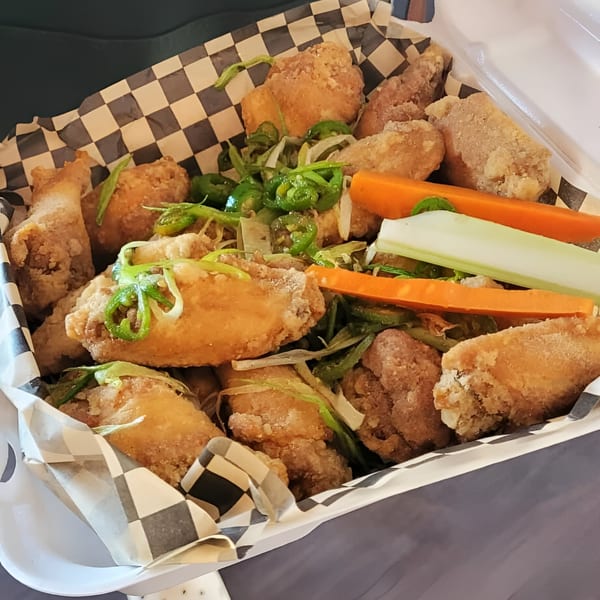 A takeout container of Knockout Wings with fried chicken, green peppers, carrots, and celery.