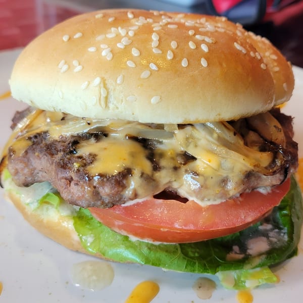 Close-up of a Knockout Wings cheeseburger with melted cheese, caramelized onions, lettuce, and tomato.