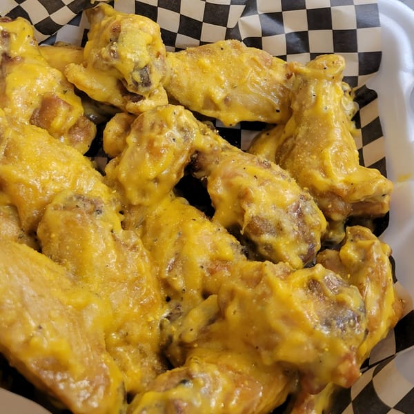 Close-up of Knockout Wings' golden-yellow, saucy chicken wings in a checkered paper liner.