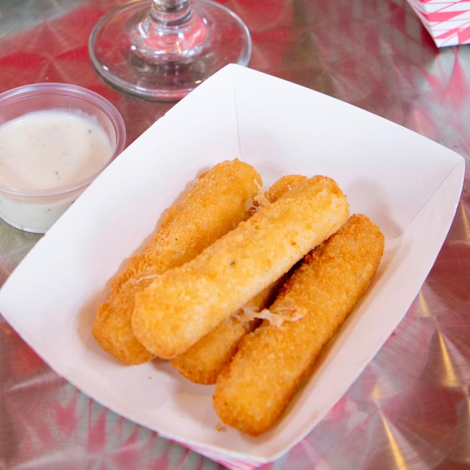 Golden-brown mozzarella sticks with melted cheese in a white paper tray, served with a side of ranch.